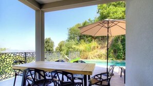 Een terras met een tafel, stoelen en een parasol, met uitzicht op een zwembad.