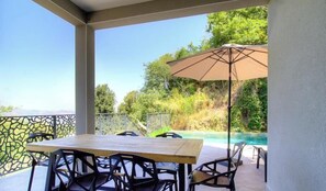 Een terras met een tafel, stoelen en een parasol, met uitzicht op een zwembad.