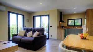 Een moderne woonkamer met een bank, een eettafel met fruit en een keukenhoek met een raam.