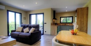 Een moderne woonkamer met een bank, een eettafel met fruit en een keukenhoek met een raam.