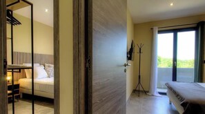 Een hotelkamer met een bed, een bureau, een kapstok en uitzicht op groen.