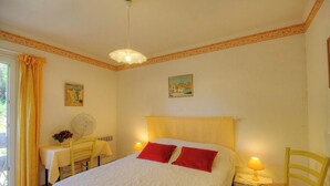 Ein Schlafzimmer mit einem Bett, zwei Nachttischlampen, einem Ventilator, einem Tisch mit Stuhl und zwei Bildern an der Wand.