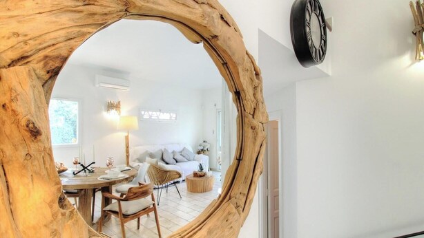 Una sala de estar con un espejo redondo de madera, un sofá blanco, una mesa de comedor con sillas y un reloj en la pared.