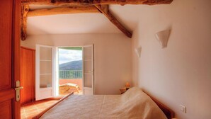 Ein Schlafzimmer mit Bett, Holztür, Balkon mit Aussicht und einem kleinen Tisch mit Lampe.