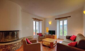 Ein Wohnzimmer mit Kamin aus Stein, einem Fernseher und einer Couch mit roten Kissen.