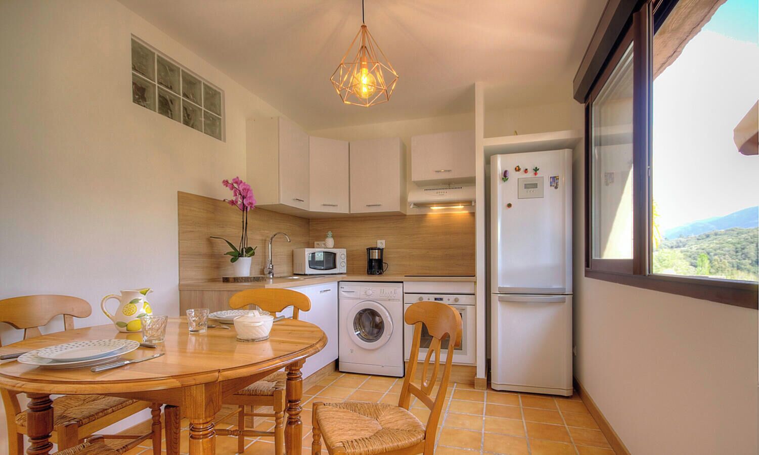 A compact kitchen with a dining table, chairs, a washing machine, a microwave, and a refrigerator.