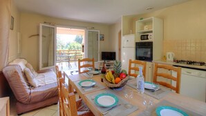Un comedor con una mesa dispuesta para dos personas, un sofá y una cocina equipada con microondas y estufa.