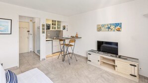 Un espacio habitable compacto con kitchenette, zona de comedor con mesa y sillas plegables, televisor de pantalla plana y un cuadro en la pared.