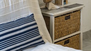 Una cama con un cojín a rayas blanco y azul, una lámpara sobre una mesita de noche de madera y cestos de mimbre.
