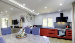 A modern kitchen with a dining area, a clock on the wall, and a window providing natural light. - Le Milan - PORTO VECCHIO (PORTO VECCHIO)