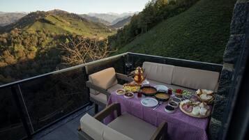 A balcony with a table set for a meal, overlooking a mountainous landscape.