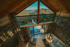 A high-ceiling room with a large window, a wooden ceiling, and a stone wall.