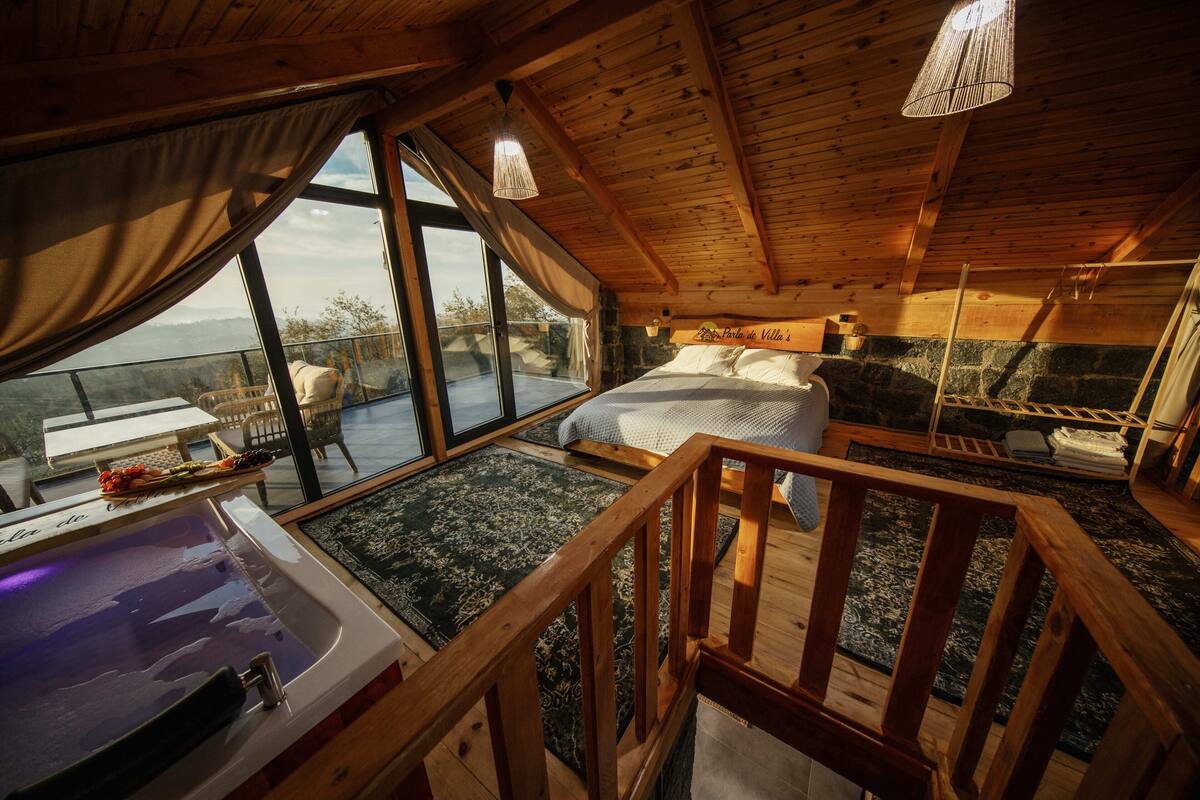 Una cabaña de madera con una cama grande, un jacuzzi y un balcón con vistas.