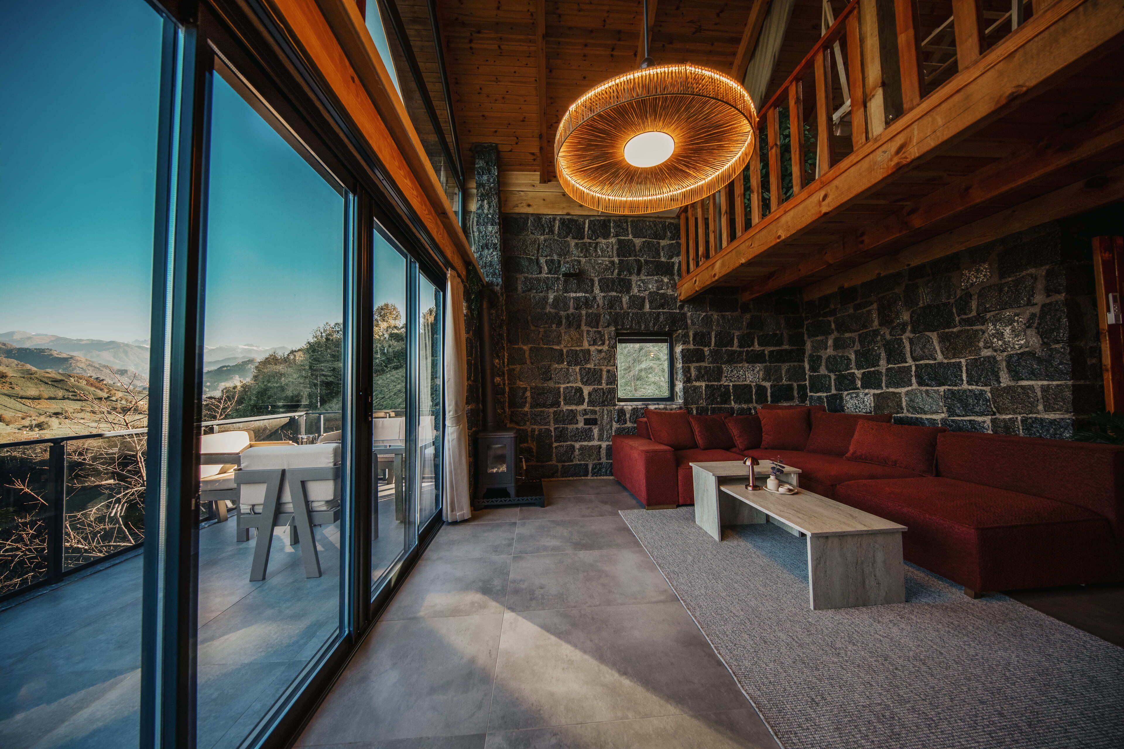 A modern interior with a stone wall, a red sofa, and a large window overlooking a mountainous landscape.