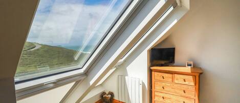 A room with a sloped ceiling, a wooden dresser, a radiator, and a view of a coastal landscape through a skylight.