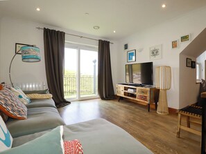 A living room with a sofa, TV, and a balcony with curtains. - Lowenna (Newquay)
