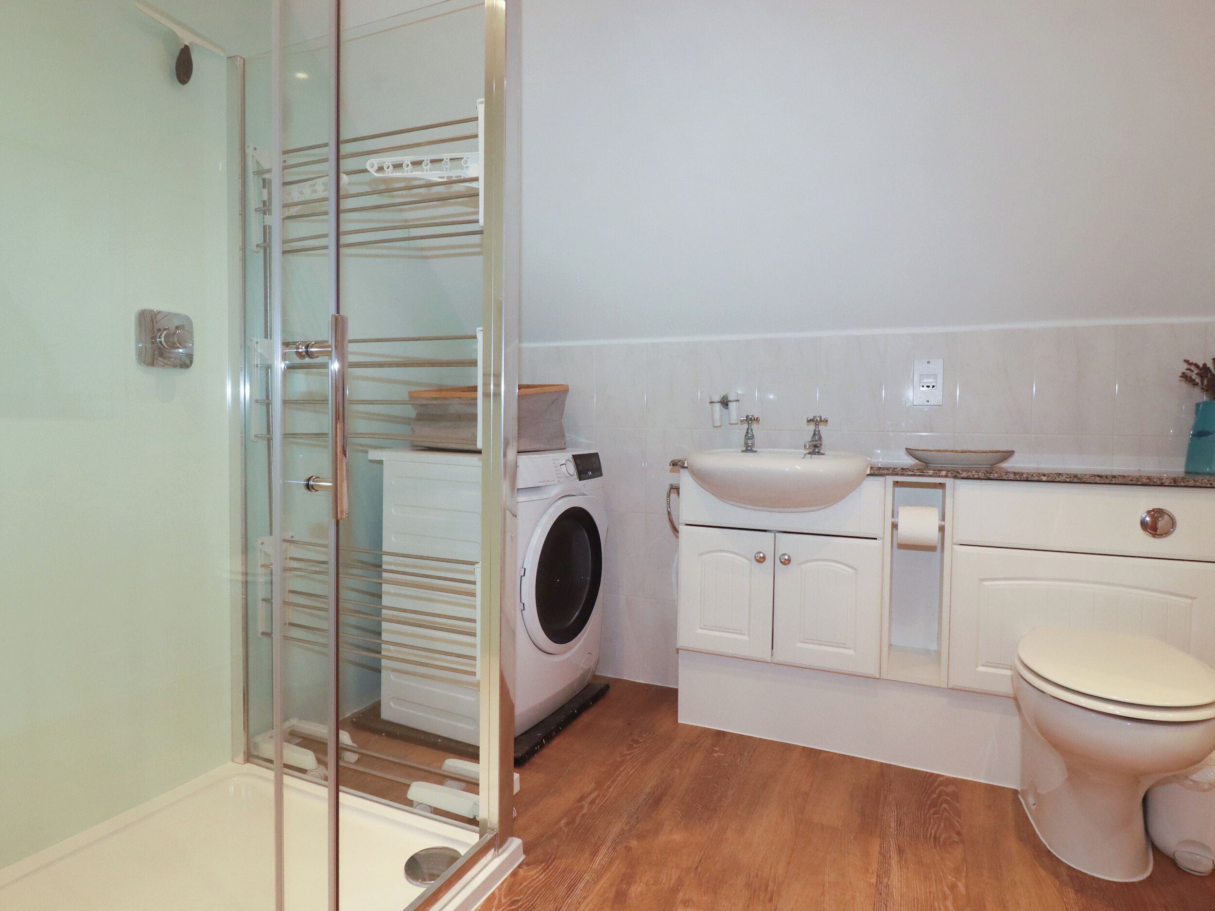 A bathroom with a glass shower enclosure, a washing machine, a sink, and a toilet.