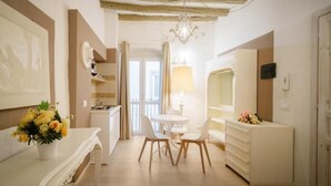 A room with a dining table, chairs, a chandelier, a white dresser, and a mirror. - Oisife Apartments (Cagliari)
