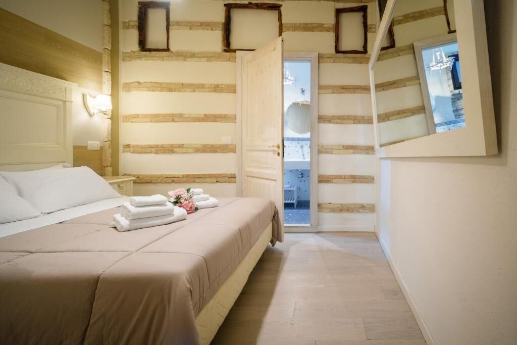 A bedroom with a bed, a nightstand, a wall-mounted light, and a door leading to a balcony.
