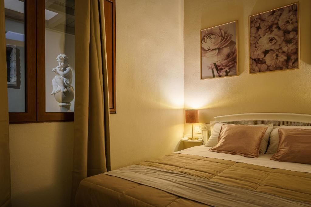 Una habitación de hotel con cama, mesita de noche, lámpara y dos cuadros florales colgados en la pared.