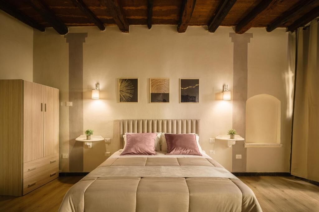 A bedroom with a large bed, wooden wardrobe, bedside tables, and wall-mounted lights.