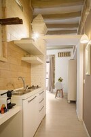 Cucina stretta con lavello, pensili e piano di lavoro. Una porta conduce in un'altra stanza.