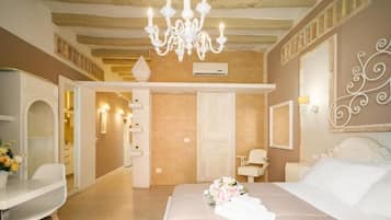 A bedroom with a bed, a chandelier, a white dresser, and a bathroom with a shower.