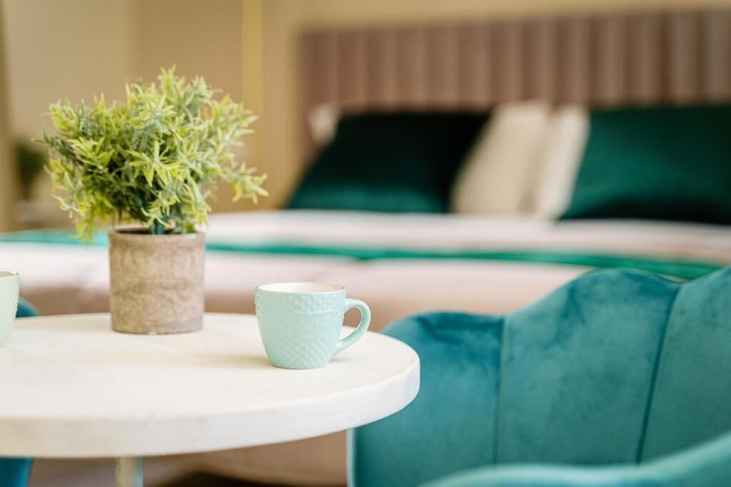 Una cama con cabecera verde, una planta pequeña en maceta y un sofá color verde azulado.