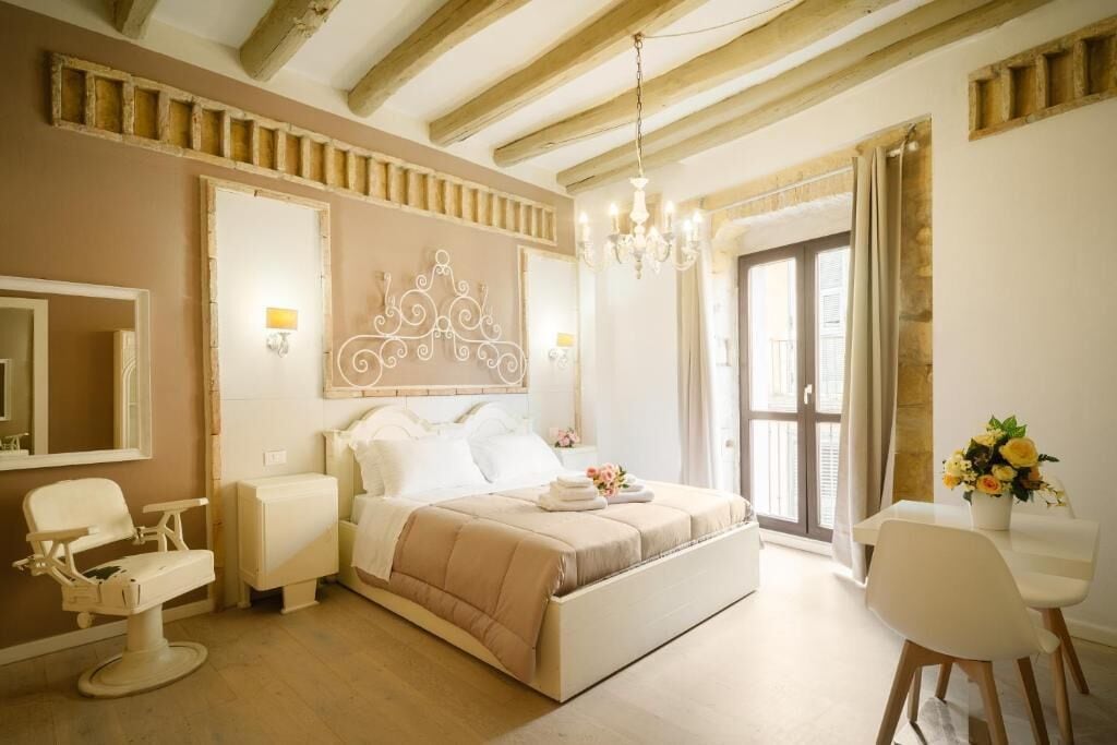 A bedroom with a bed, bedside table, chair, and a large mirror.