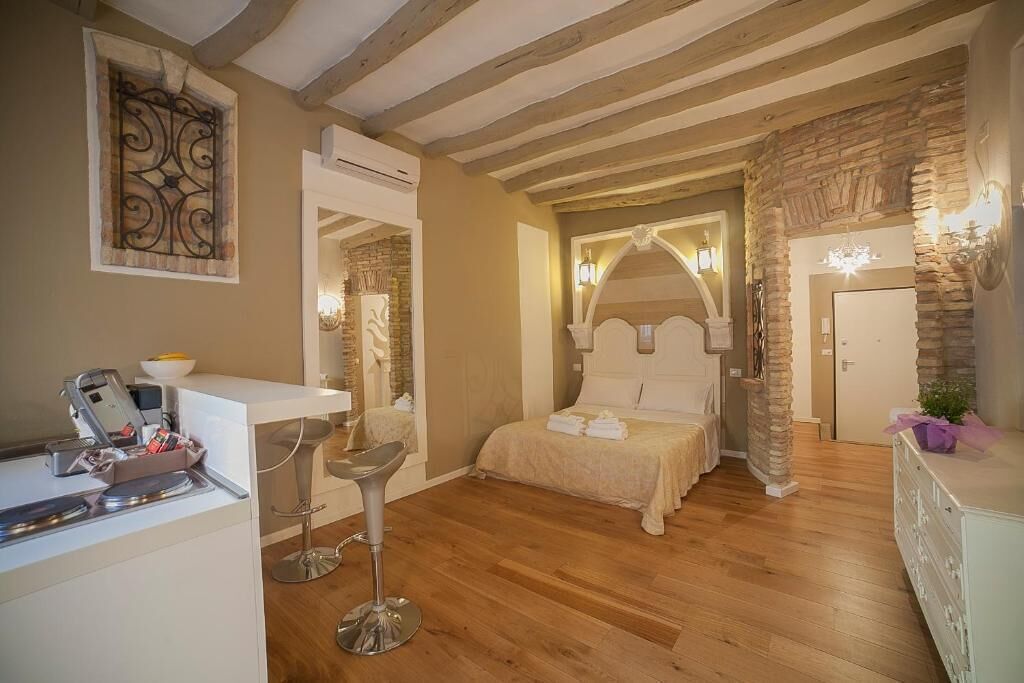 Une chambre avec un lit, un bureau avec un ordinateur, une chaise et un mur en pierre.