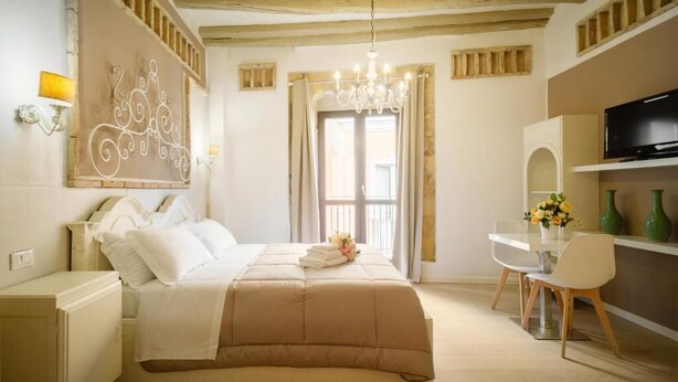 A bedroom with a bed, a desk, a chair, a TV, and a chandelier. - Oisife Apartments (Cagliari)