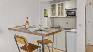 Cocina compacta con una mesa de comedor, dos sillas, una botella de vino y un microondas.