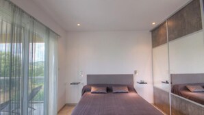 A modern bedroom with a large bed, a sliding glass door to a balcony, and a mirrored closet. - L'Ogliastru - SOLLACARO (SOLLACARO)
