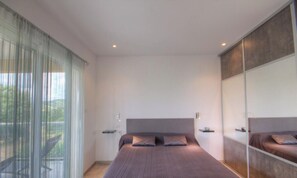 Ein modernes Schlafzimmer mit einem großen Bett, einer Schiebetür zum Balkon und einem Spiegelkleiderschrank.