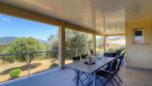 A covered outdoor balcony with a table and chairs, overlooking a landscape with trees and distant hills. - L'Ogliastru - SOLLACARO (SOLLACARO)