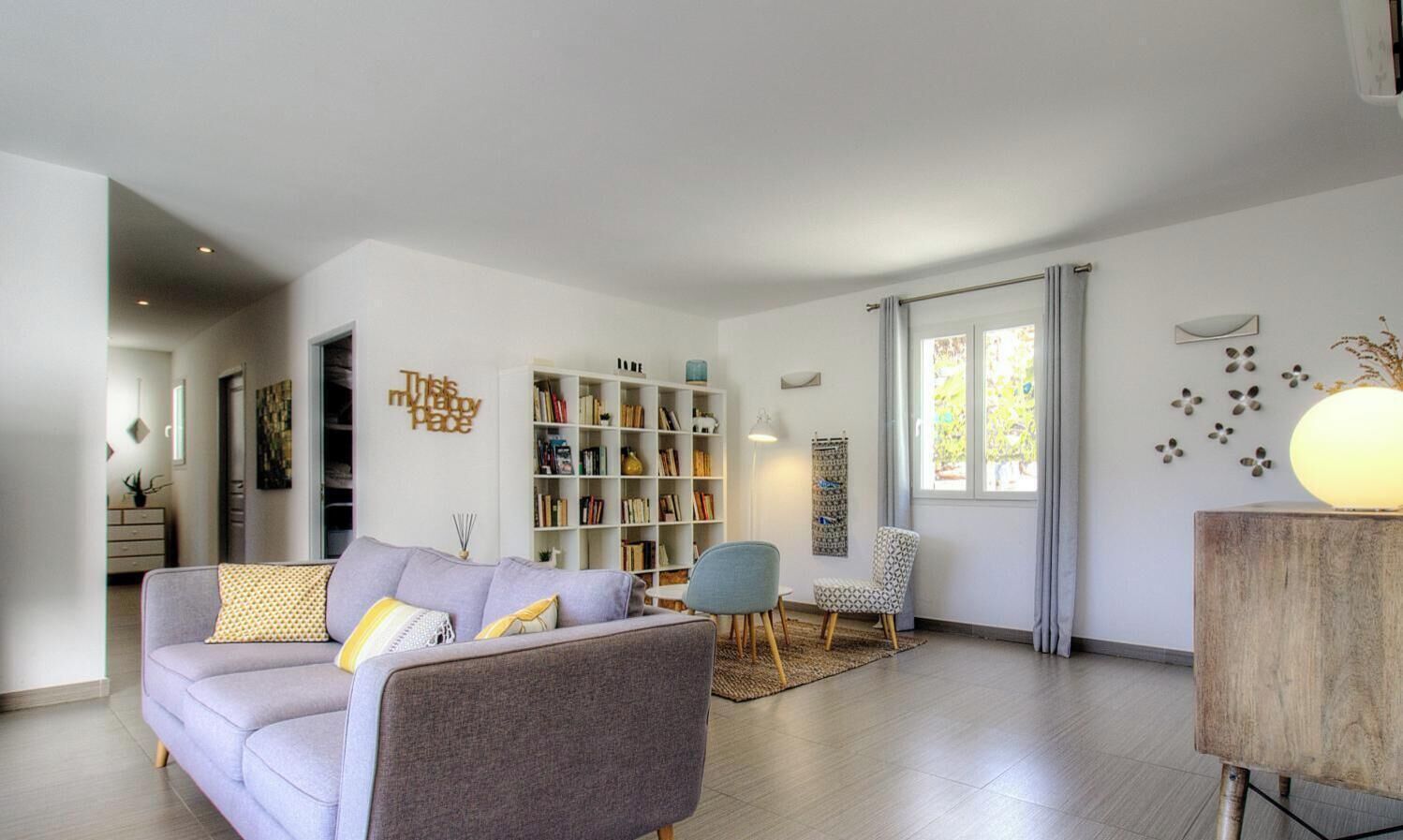 Una sala moderna con un sofá gris, una estantería, una mesa de centro y una lámpara.