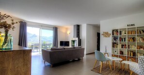 A modern living room with a sofa, a bookshelf, a TV, and a view of the outdoors. - Le 60501 - MONTEGROSSO (MONTEGROSSO)