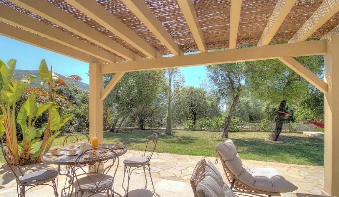 An outdoor patio with a pergola, stone flooring, metal chairs, and a table set for dining.