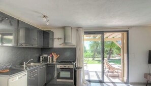 Eine moderne Küche mit Einbauofen, Spüle und Herd. Eine Schiebetür aus Glas führt zu einem Außenbereich mit Terrasse und einem Stuhl.