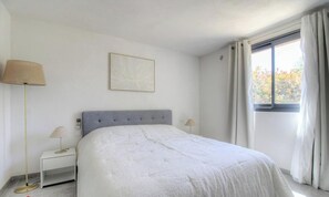 Ein Schlafzimmer mit Bett, Nachttischen, einer Lampe, einem Fenster mit Vorhängen und einem Wandbild.