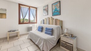 Ein Schlafzimmer mit einem Bett, einem Nachttisch, einer Lampe, einem Fenster und einer Wand mit einem gerahmten Bild.