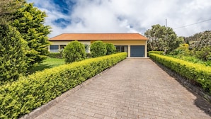 A building with a paved pathway leading to a door, surrounded by well-maintained hedges and trees. - Sweet Orchard Escape - By Wehost (Porto Moniz)