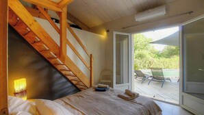 Ein Schlafzimmer mit einer Holztreppe, einem Bett, einem Fenster und Blick auf eine Terrasse.