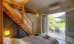 Ein Schlafzimmer mit einer Holztreppe, einem Bett, einem Fenster und Blick auf eine Terrasse.