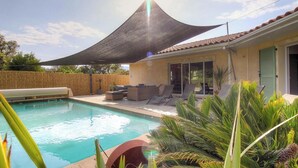 Ein Schwimmbecken mit Liegestühlen und Sonnenschirm, umgeben von tropischen Pflanzen.