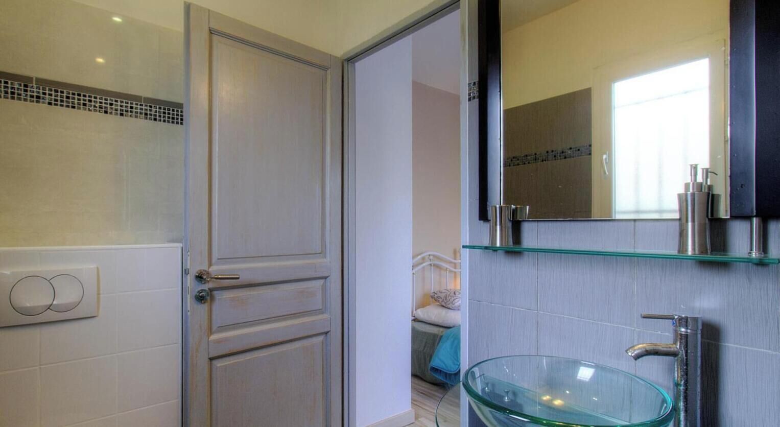 A bathroom with a glass bowl sink, a mirror above it, and a door with a handle.