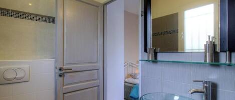 A bathroom with a glass bowl sink, a mirror above it, and a door with a handle.
