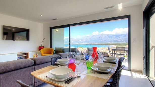 A dining area with a table set for four, a sofa, and a TV mounted on the wall. - Casa Di l'Alba - CALVI (CALVI)