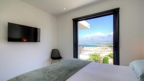 A bedroom with a bed, a chair, a TV, and a window with a mountain view. - Casa Di l'Alba - CALVI (CALVI)
