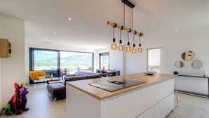 A modern kitchen with a central island, a dining area with a sofa and chairs, and large windows offering a view of the outdoors. - Casa Di l'Alba - CALVI (CALVI)